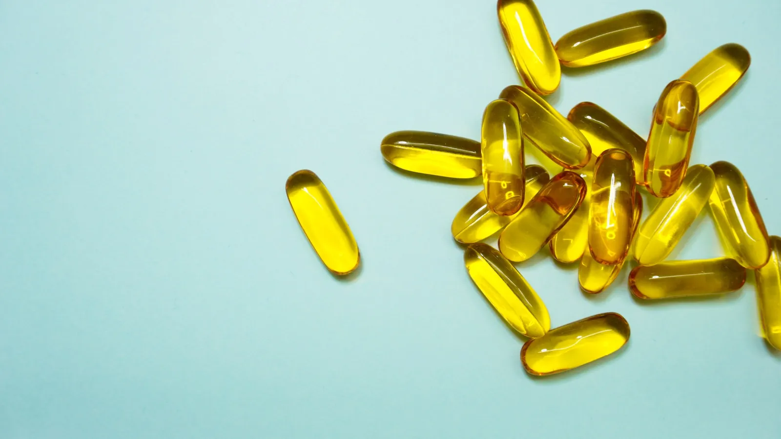 Gele supplementcapsules op een lichtblauwe ondergrond.