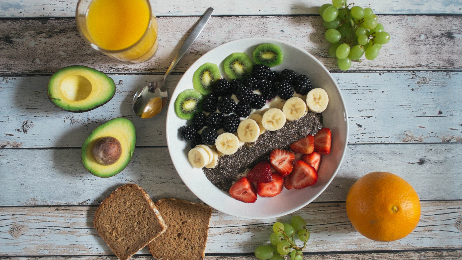 Een kom met vers fruit, avocado en havermout op een houten tafel.