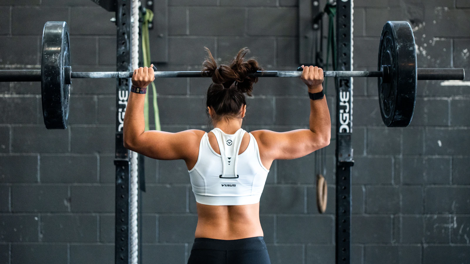Sporter tilt een barbell op schouderhoogte in een squatrek in een sportschool.