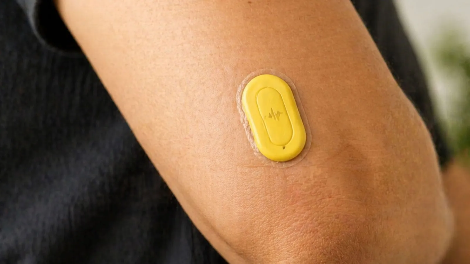 Een gele sensor zit op de bovenarm van iemand in een donker T-shirt.