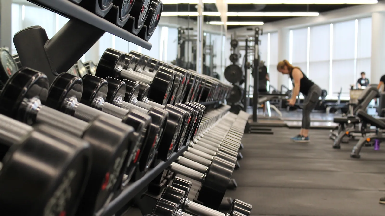 Een rek met dumbbells op de voorgrond in een sportschool.