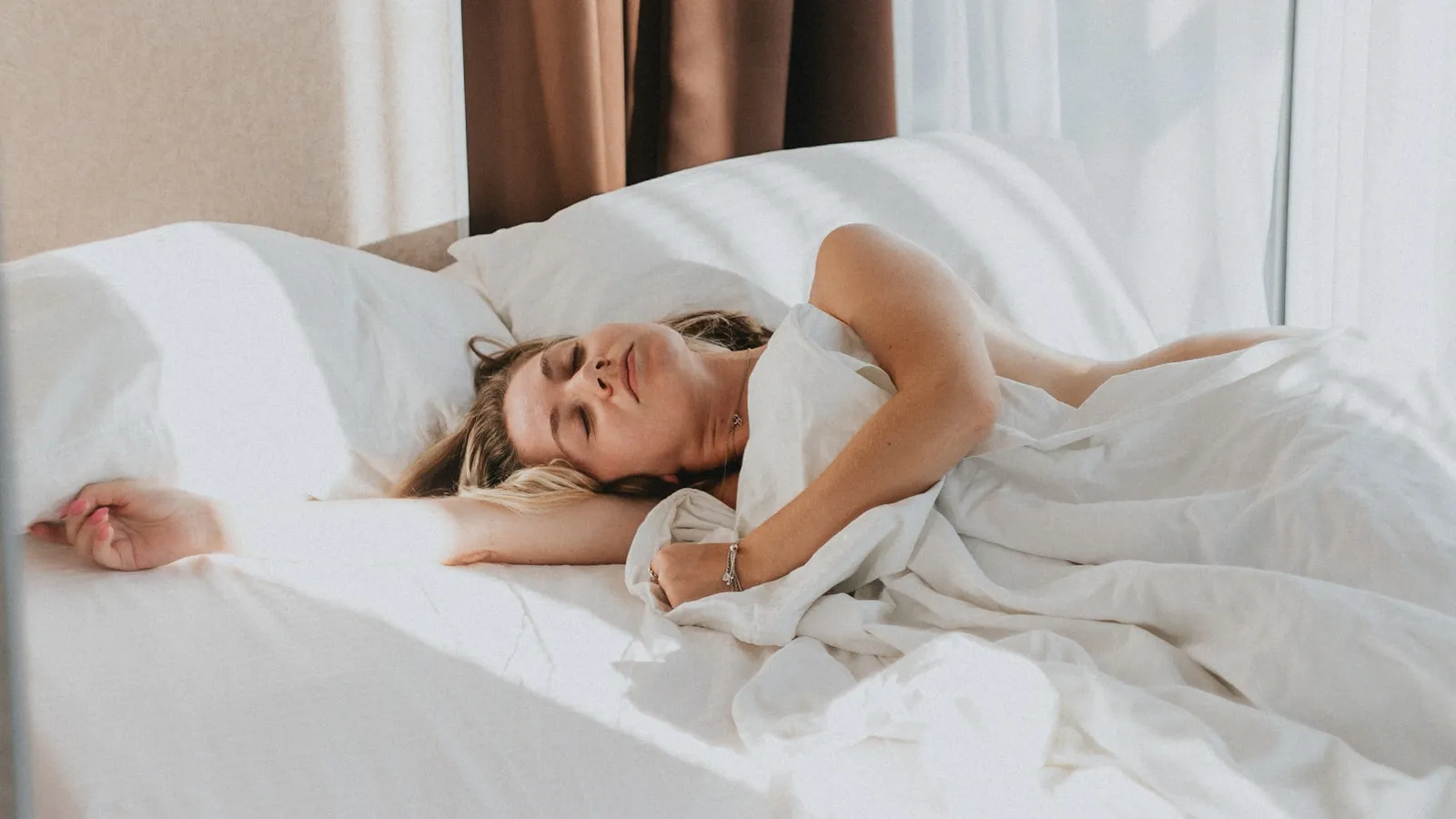 Vrouw ligt overdag uit te rusten in bed bij een licht raam.