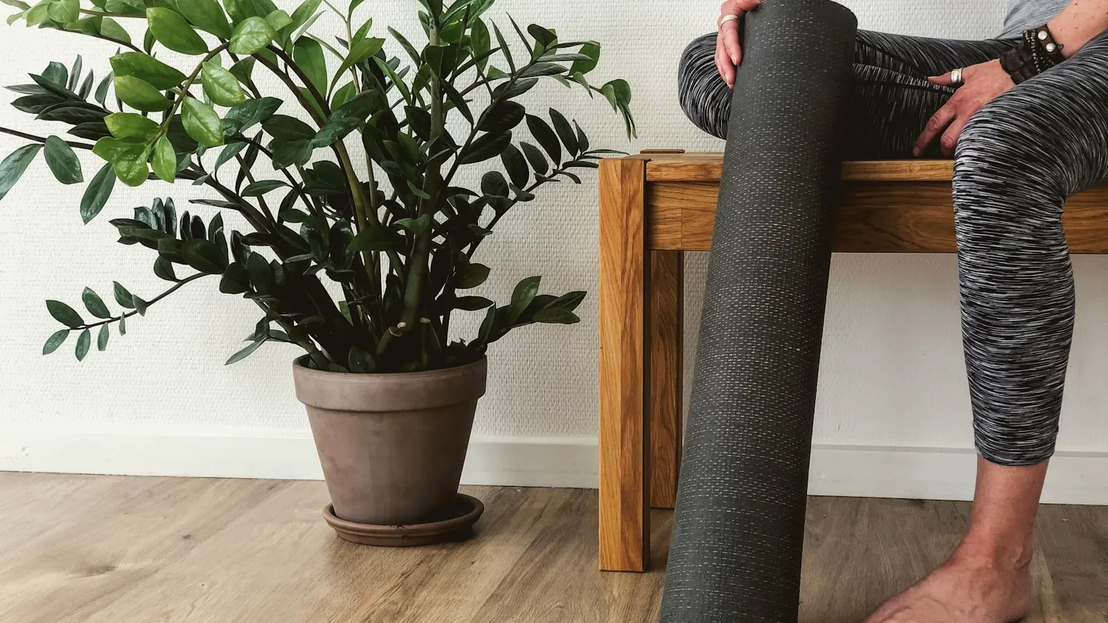 Iemand zit op een houten bank met een opgerolde fitnessmat in de hand.