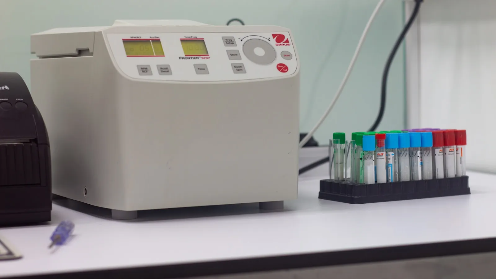 Een centrifuge naast een rek met bloedbuisjes op een laboratoriumtafel.
