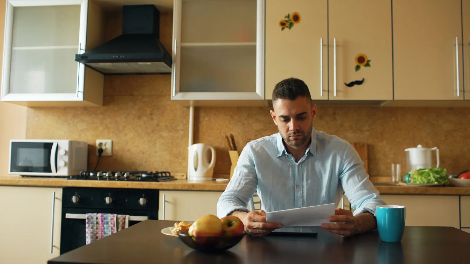 Een man leest een document aan de keukentafel, met een schaal fruit en een mok voor zich.