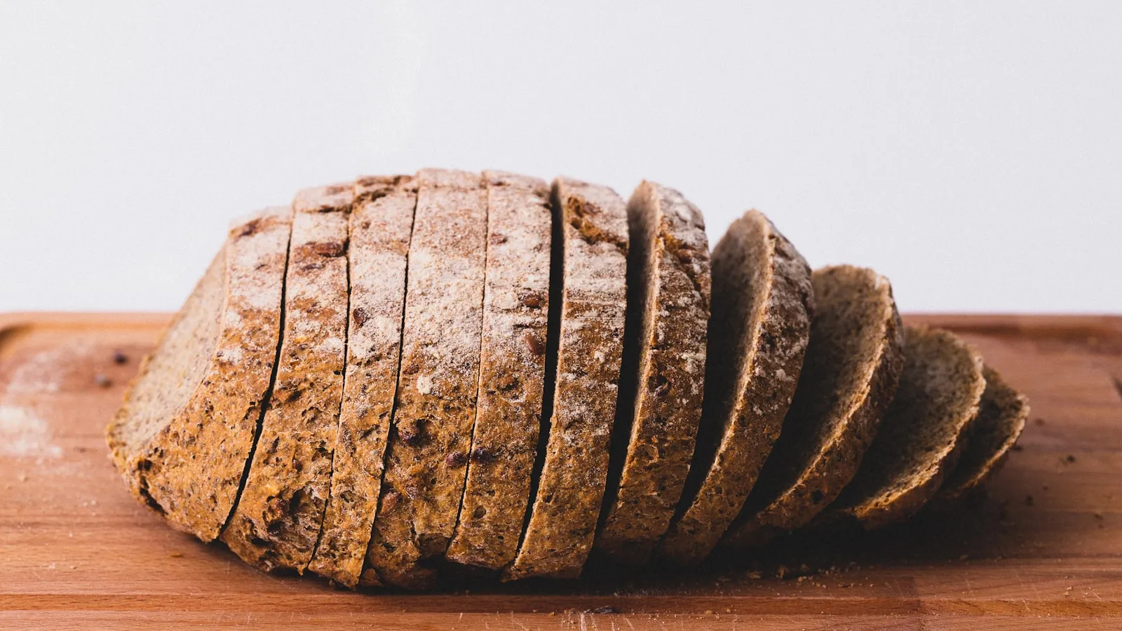 Een donker volkorenbrood in plakken gesneden op een houten plank.