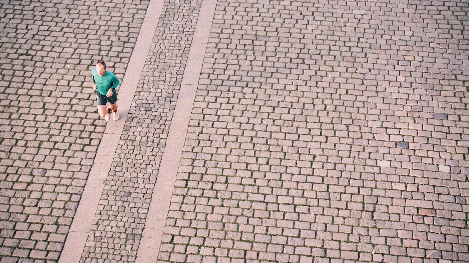 Een hardloper in een groen shirt loopt over een geplaveide straat, van bovenaf gezien.