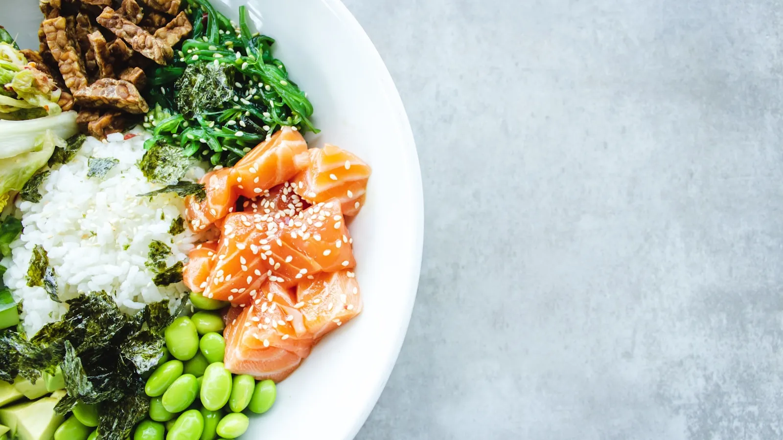 Eiwitrijke maaltijd met zalm, edamame, zeewier en rijst in een witte kom.
