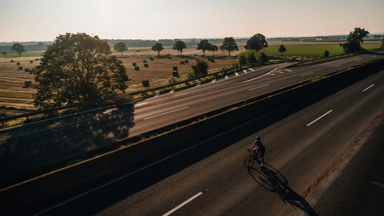 Wielrenner rijdt alleen op een lege weg door polderland bij zonsopkomst.