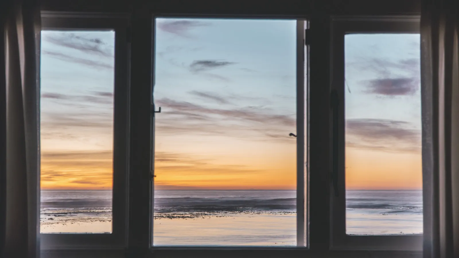 Zonsopkomst boven het water, gezien door een openstaand raam.