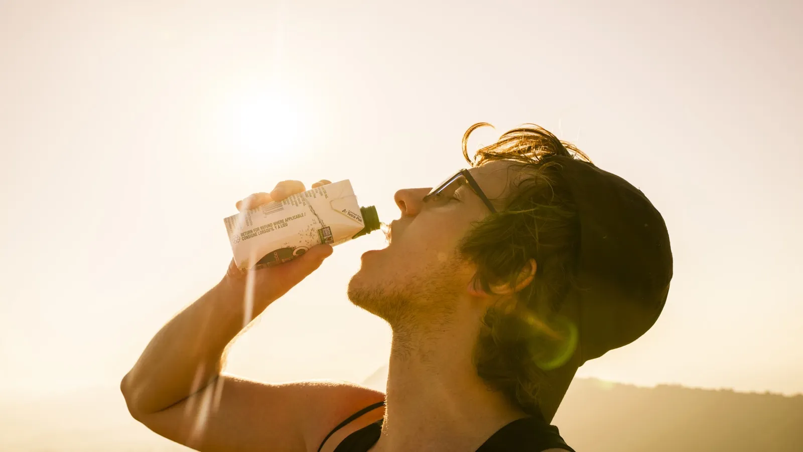 Sporter drinkt buiten iets uit een pak in het felle tegenlicht van de zon.