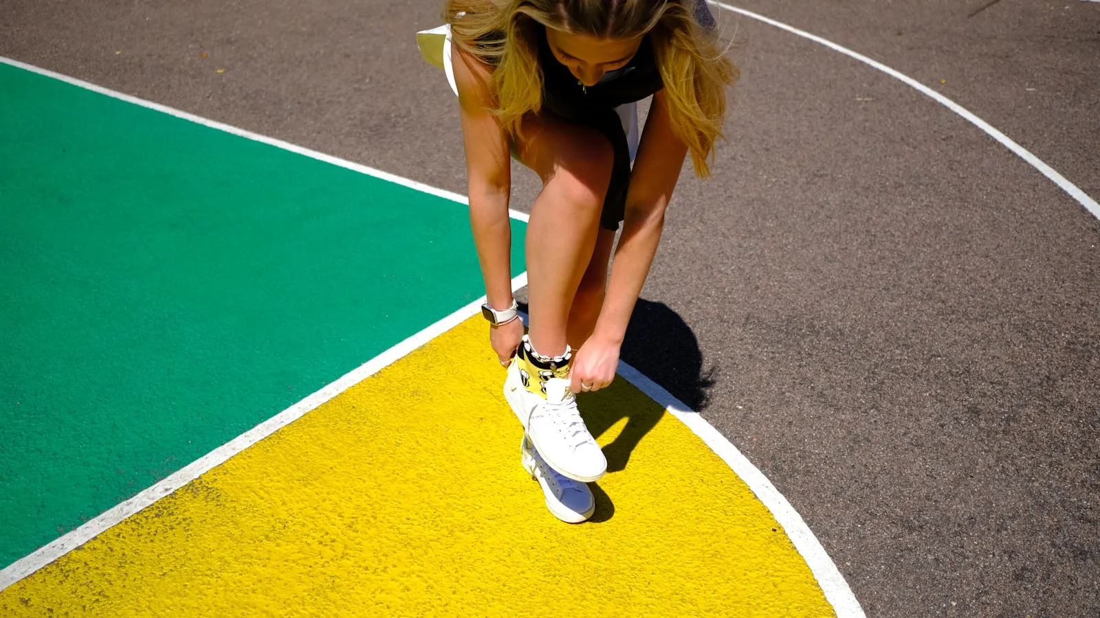 Vrouw bukt zich om haar sportschoen te strikken op een gekleurd sportveld.