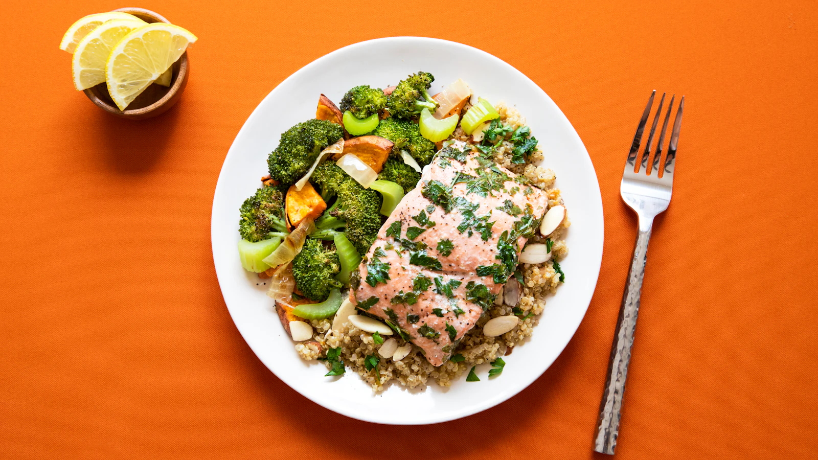 A plate with salmon, broccoli and grains on an orange background.