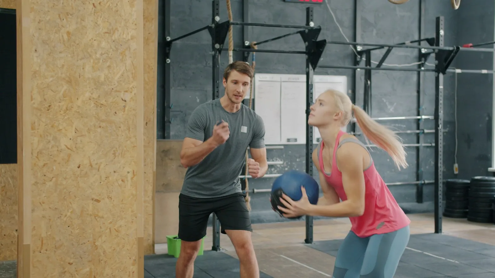 Vrouw houdt een medicijnbal vast terwijl een trainer toekijkt in een gym.