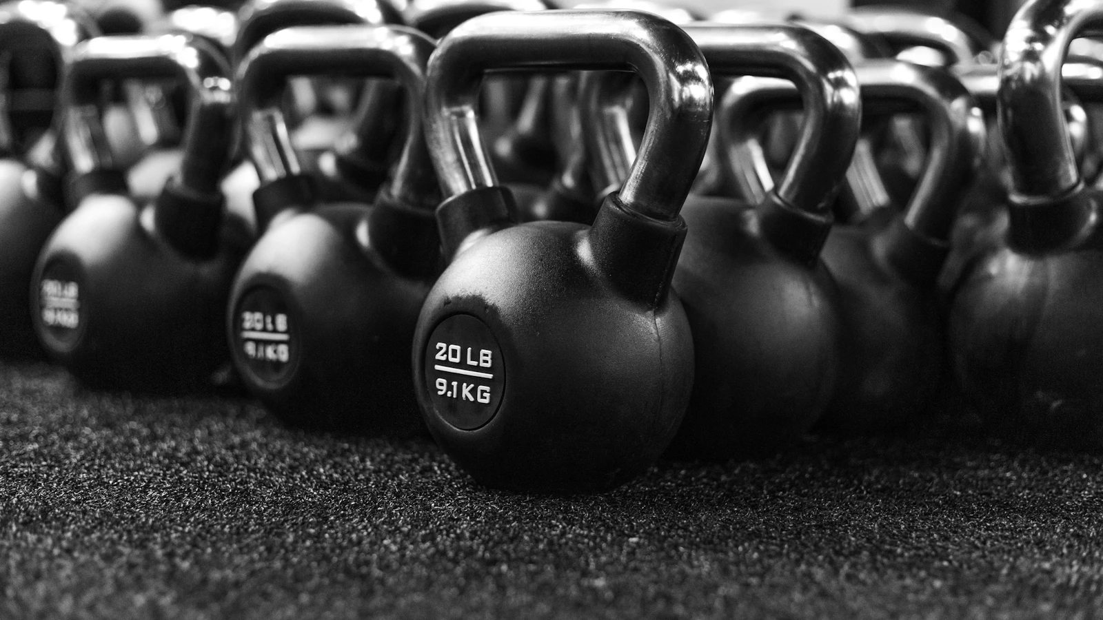 Een rij zwarte kettlebells op de vloer van een sportschool.