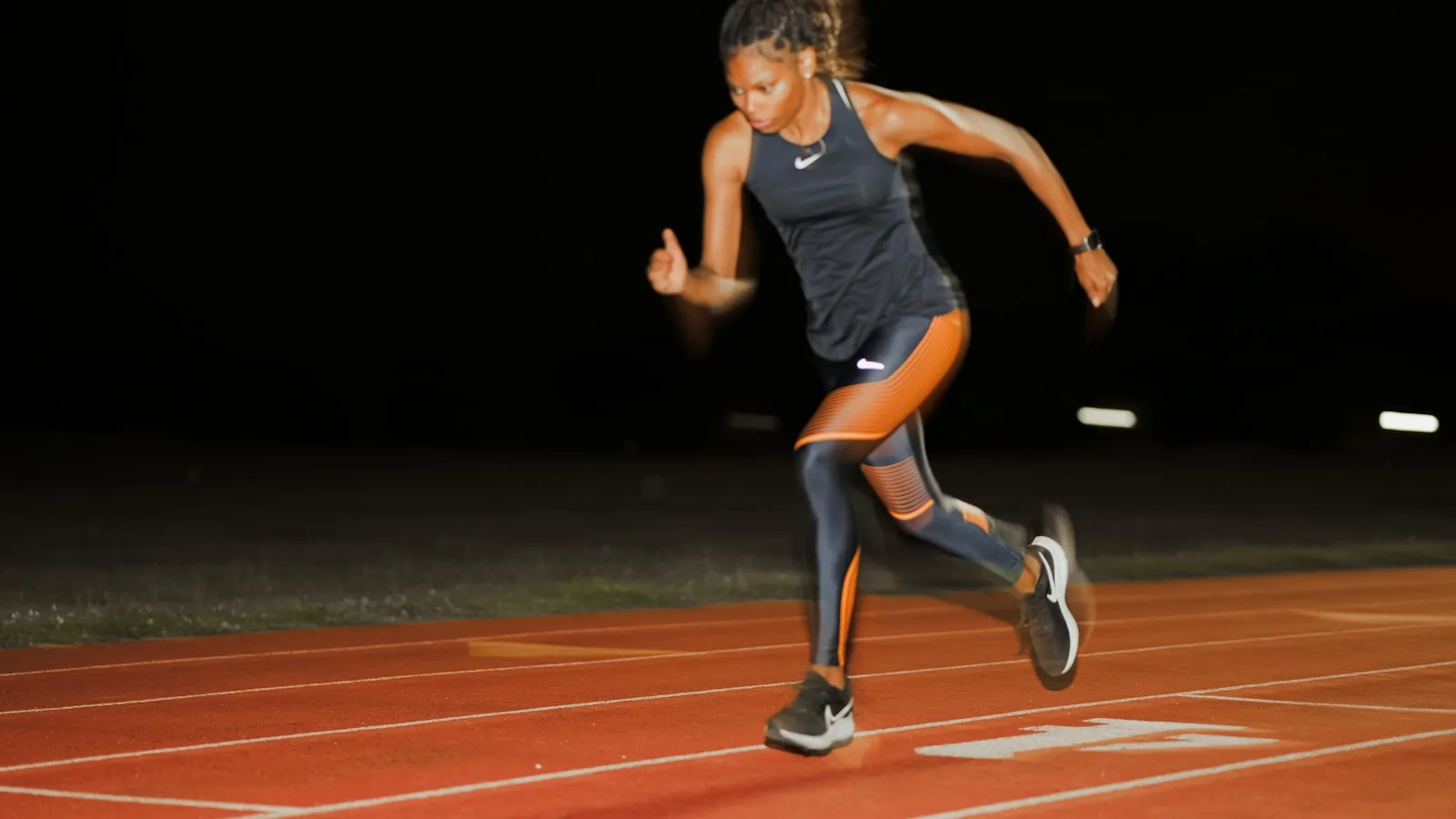 Sprintster zet aan op een verlichte atletiekbaan in het donker.