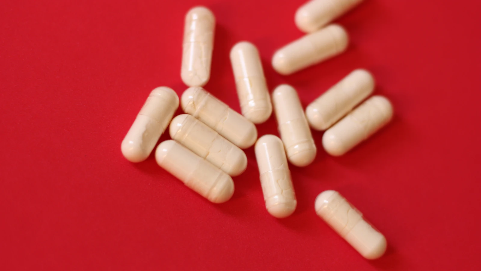 Witte capsules verspreid over een rode ondergrond.