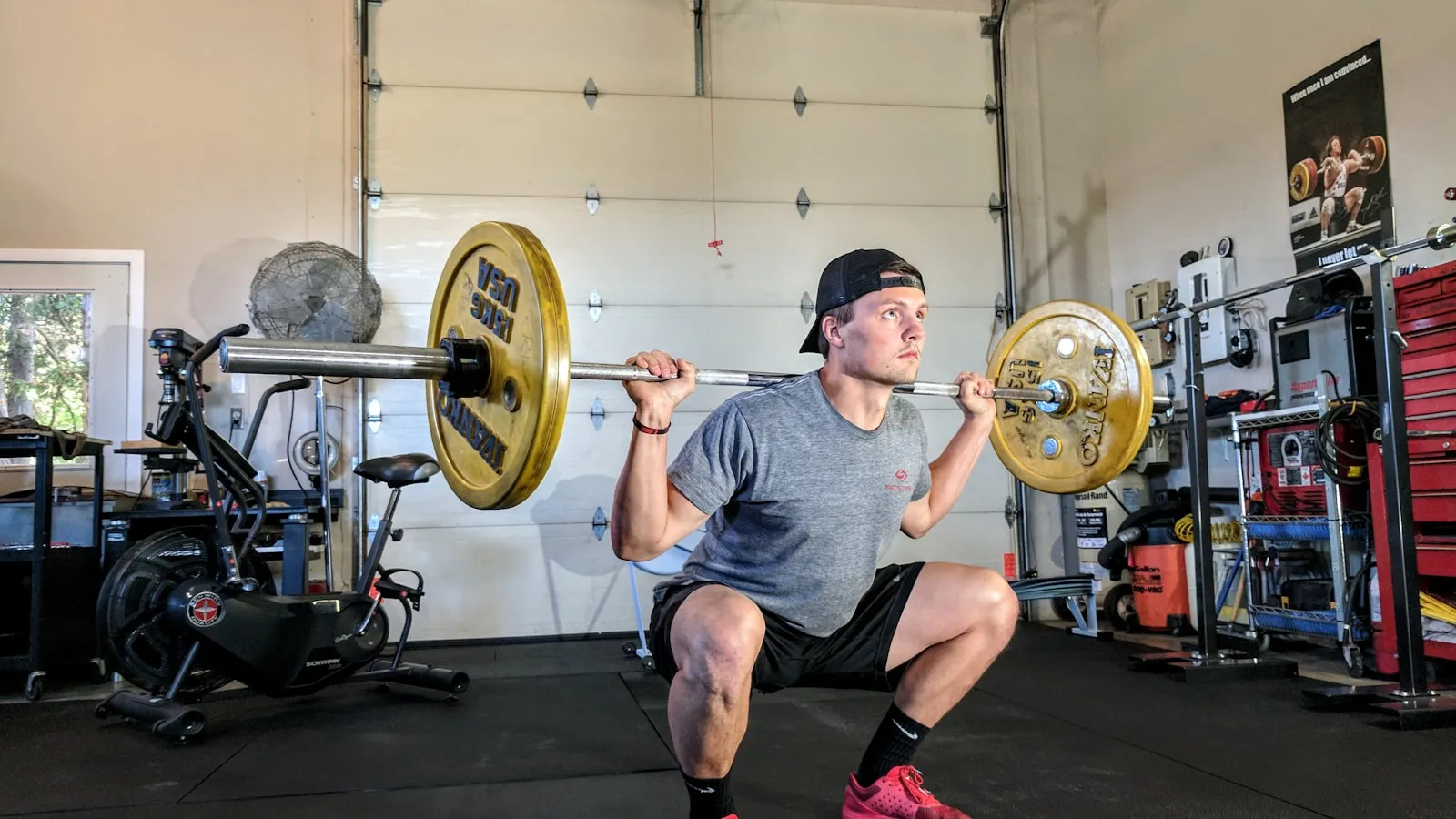 Sporter zakt door de knieen met een barbell op zijn rug in een garagegym.