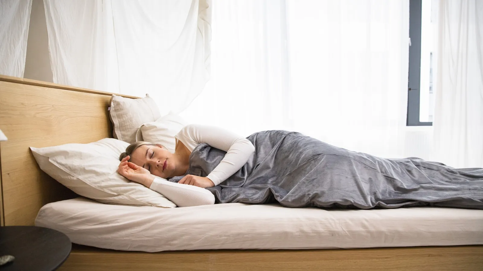 Iemand ligt te slapen in een licht slaapkamerbed onder een deken.