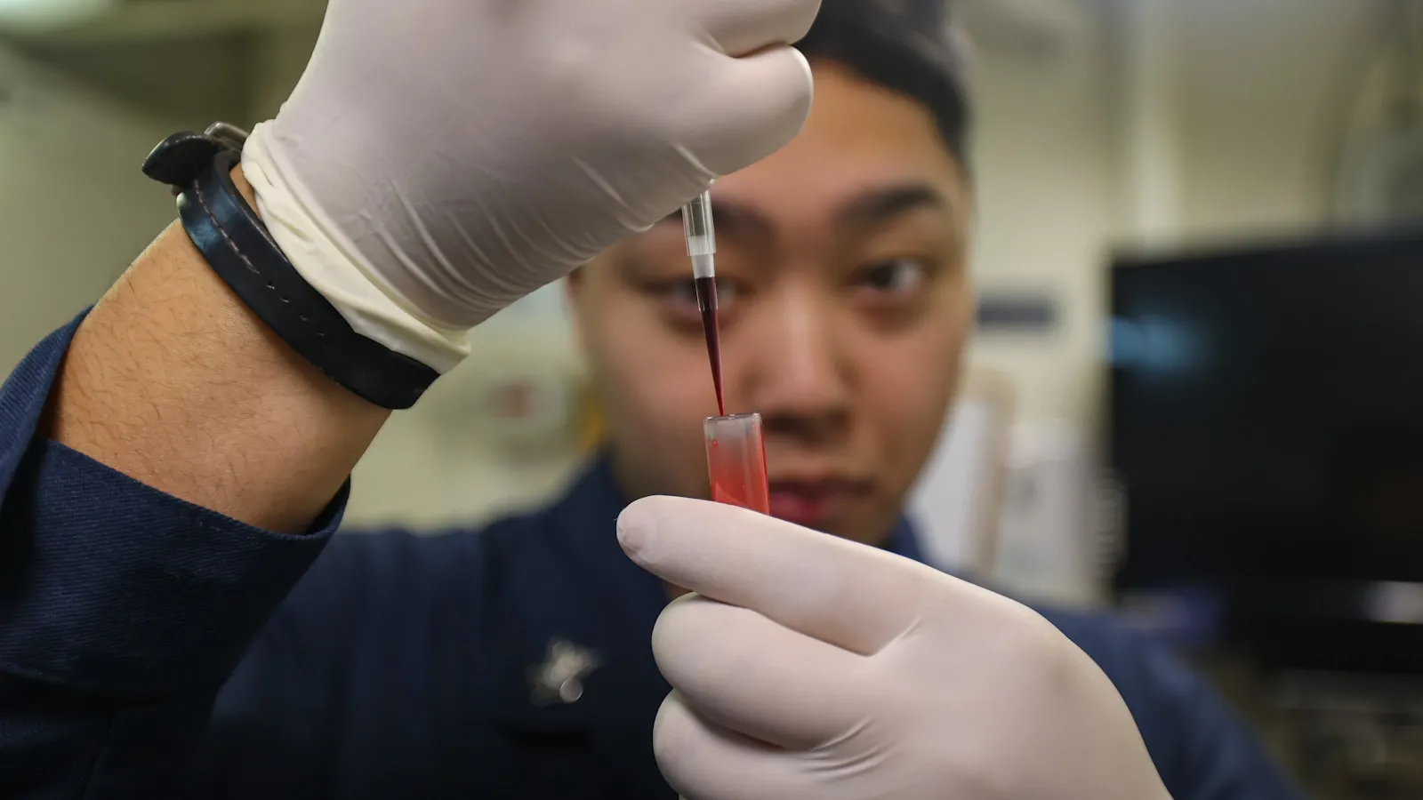 Laborant met handschoenen pipetteert vloeistof in een buisje.