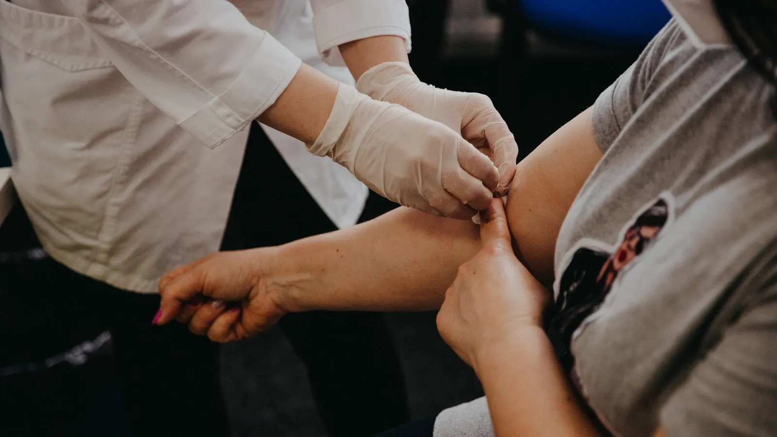 Zorgverlener met handschoenen prikt in de bovenarm van een patient.
