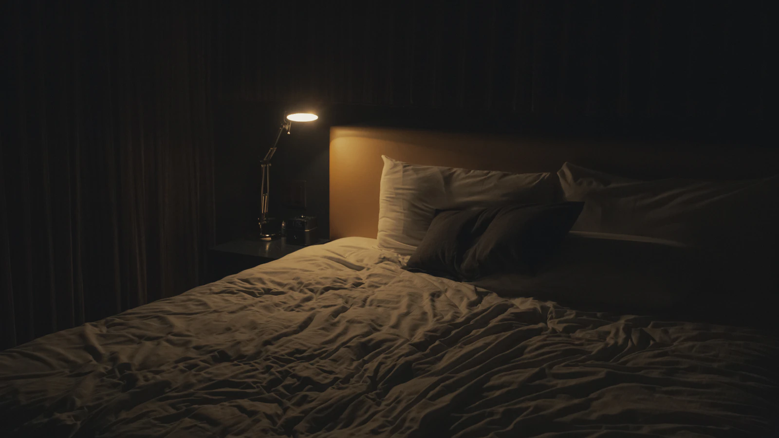 Schemerlamp naast een bed in een donkere slaapkamer.