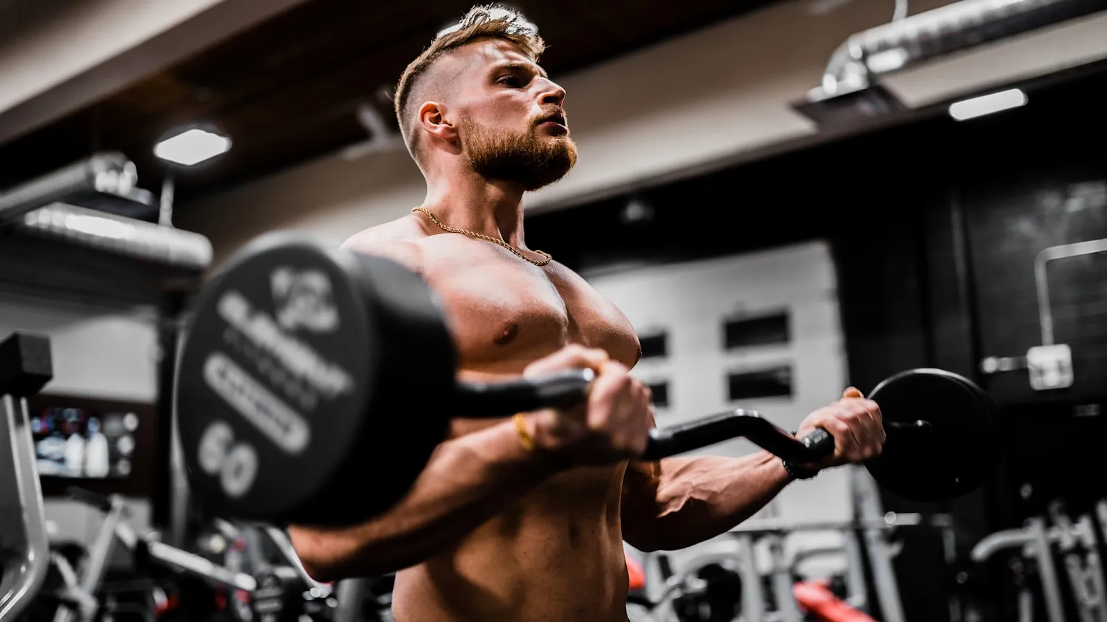 Gespierde man doet een bicepscurl met een halterstang in de sportschool.