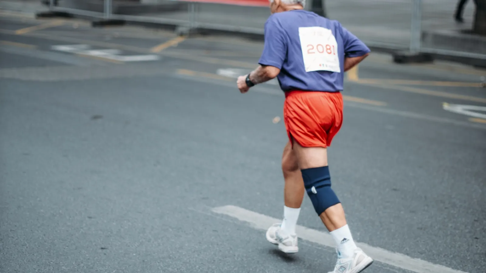 Hardloper met startnummer en kniebrace loopt over de weg tijdens een wedstrijd.